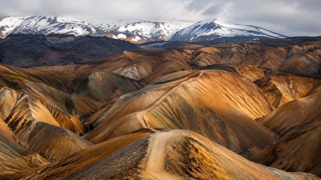 Streaked orange and green rhyolite mountains above a steaming geothermal valley on the Laugavegur
